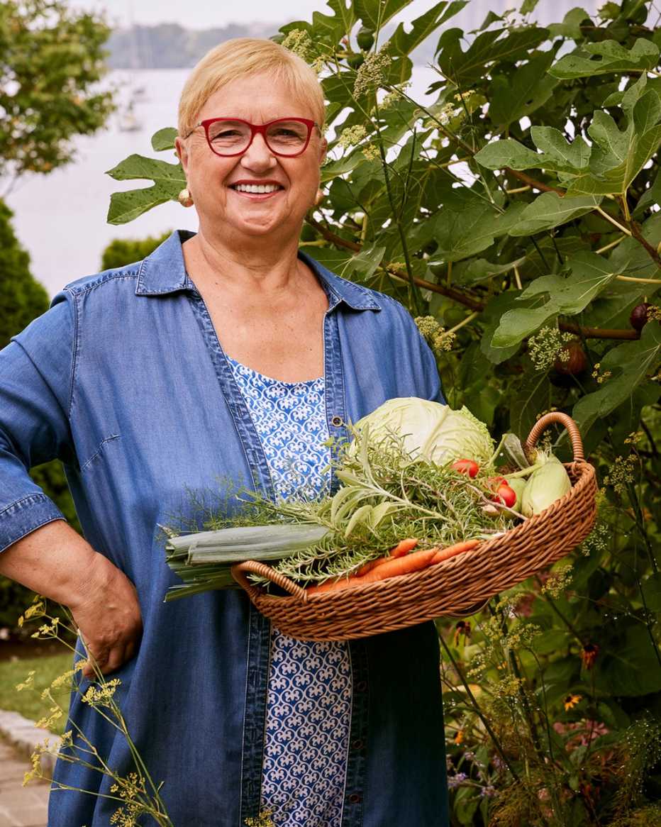 chef lidia bastianich standing in a garden holding a basket of fresh vegetables