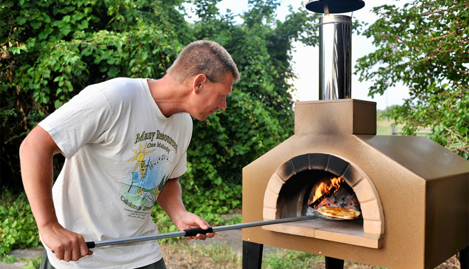 a man cooking pizza in a pizza oven in his backyard