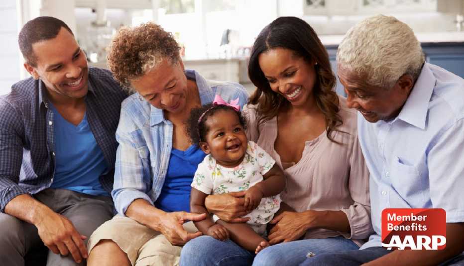 Multigenerational family sitting on a sofa with mom, dad and grandparents smiling at baby granddaughter with pink bow in her hair
