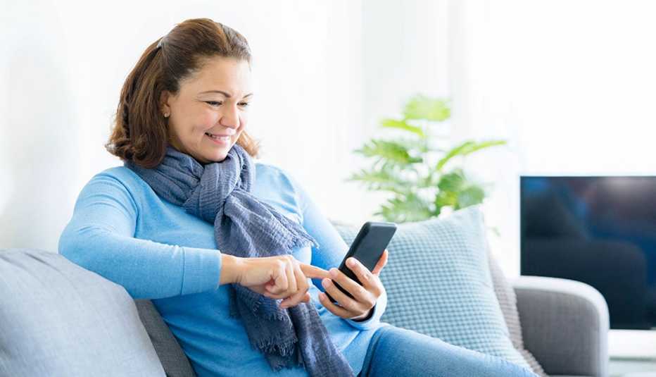A woman reading on her mobile phone smiling while sitting on a couch