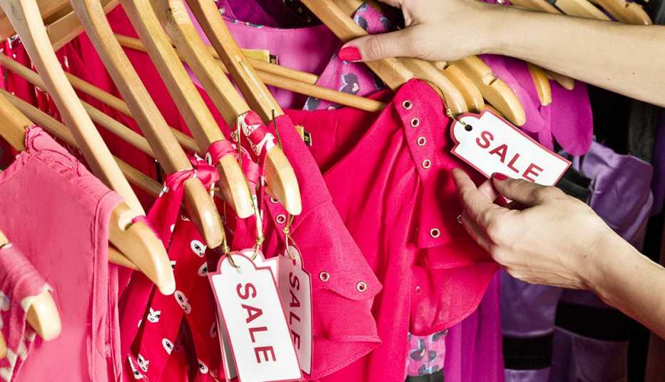 close up on the hands of a shopper looking through a store rack of pink clothing marked with sale tags