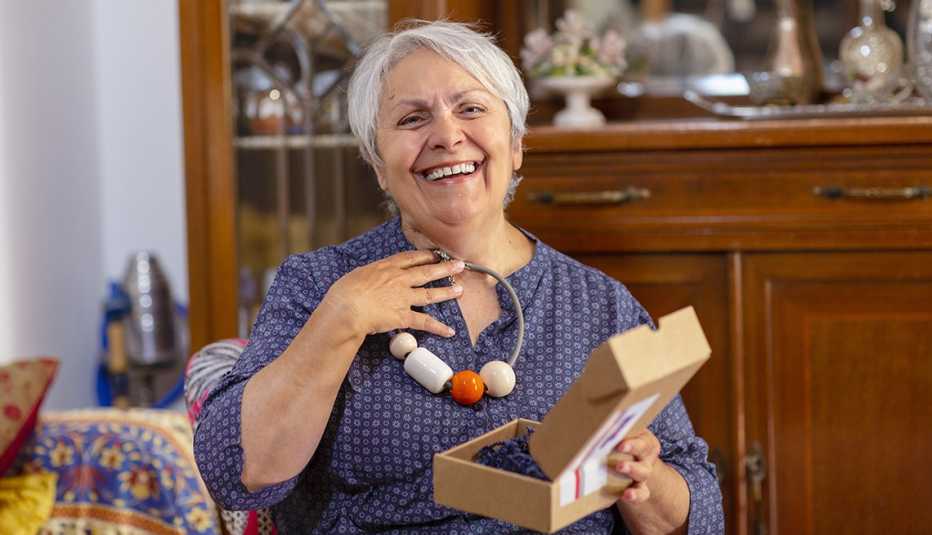 smiling woman holding up a gift necklace that was delivered to her home