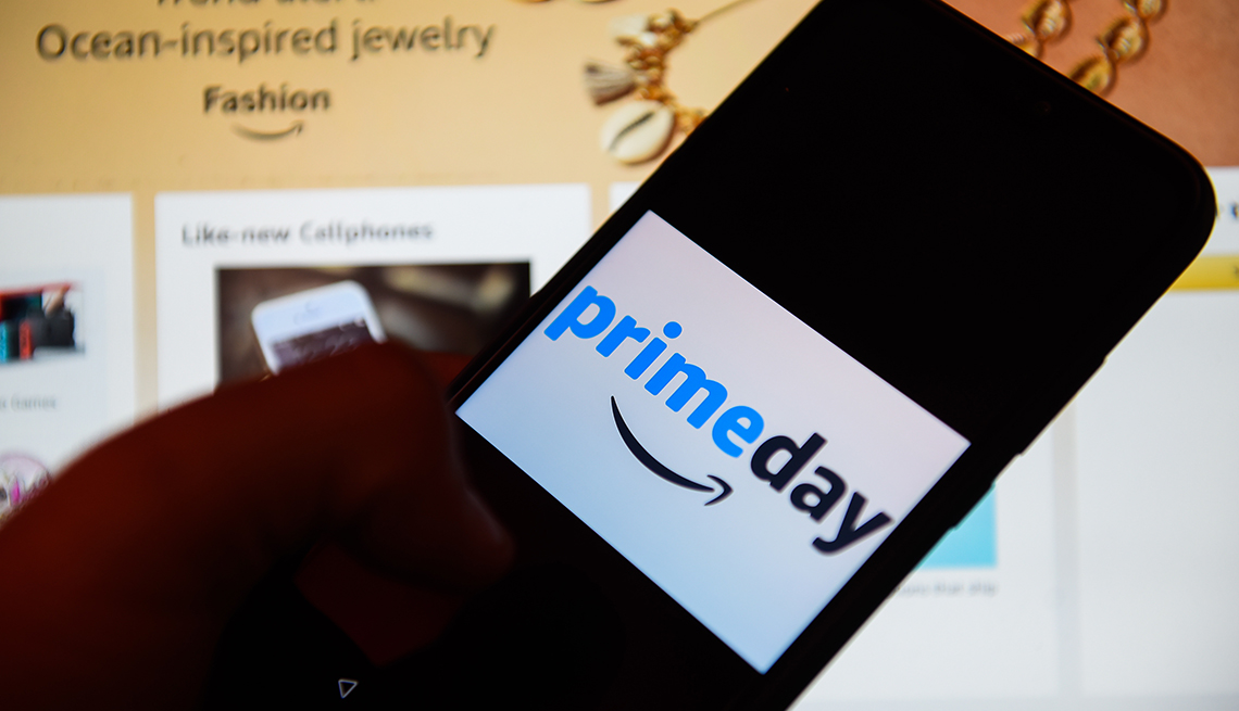 close up of a hand holding a mobile phone that says prime day against a background of an Amazon website screen shot 