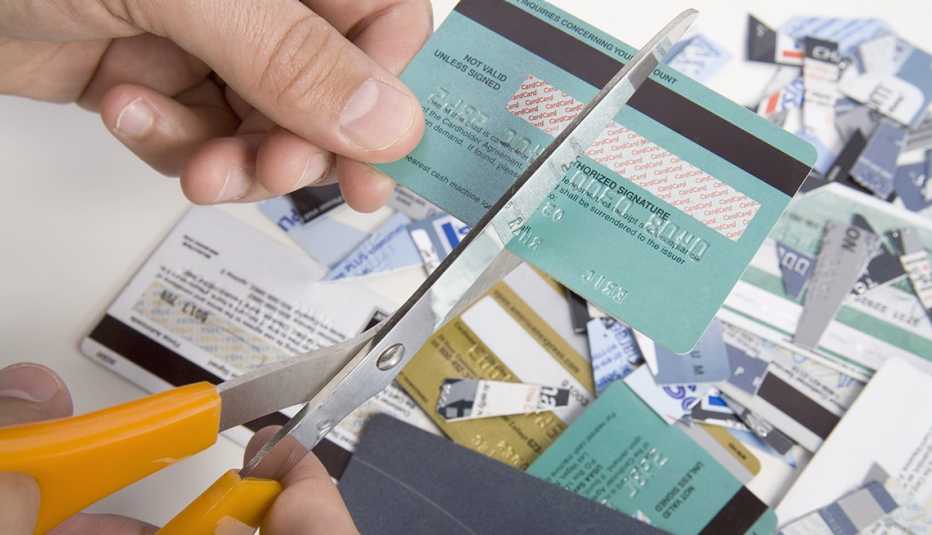 Close up of hands using scissors to cut up a credit card over pile of cut cards