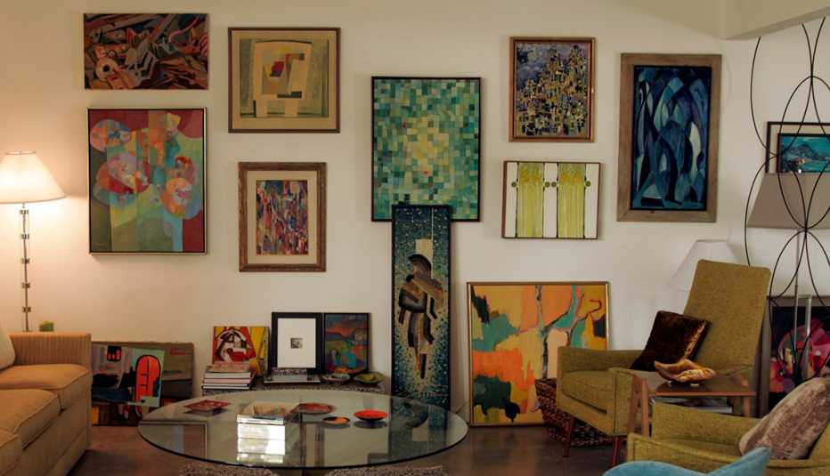 many colorful paintings hang on and lean against a wall in a living room