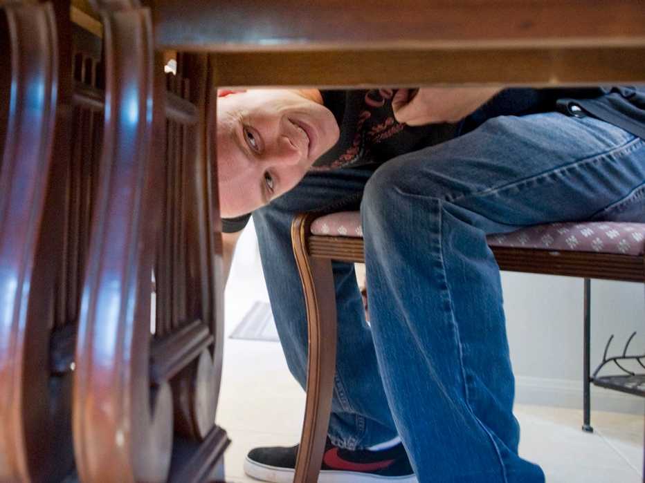 a man peeks under a dining room table to see if there is a label from the furniture maker