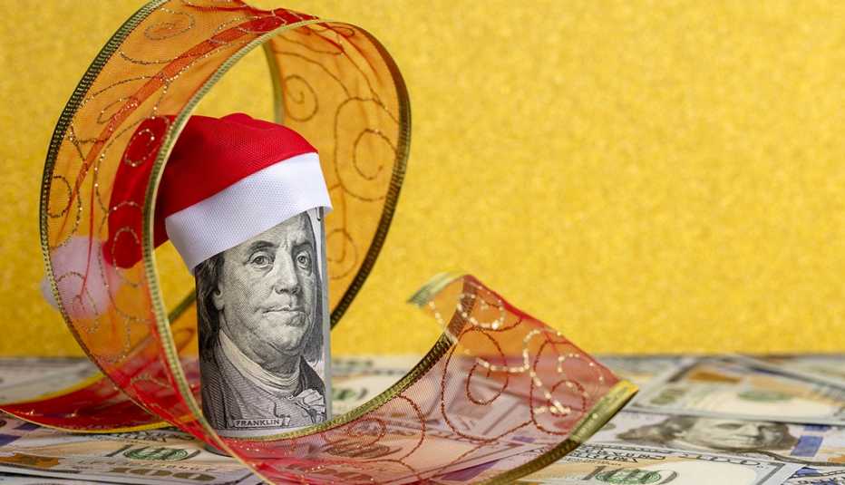 A hundred dollar roll of bills in a Santa hat on a heap of US 100 dollar bills.