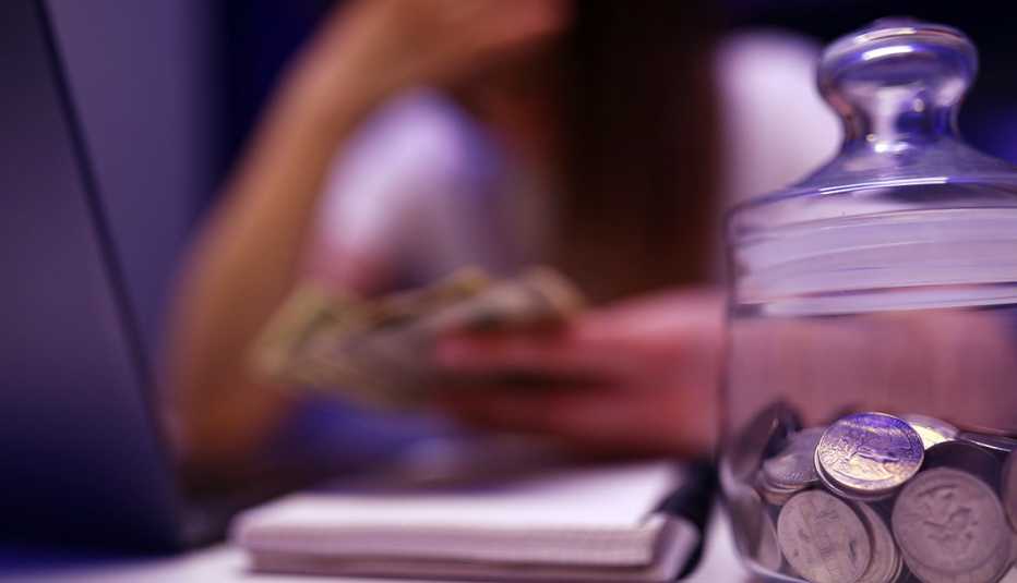 a soft focus image that looks melancholy, of a woman hunched over table holding money with jar of quarters in foreground. 
