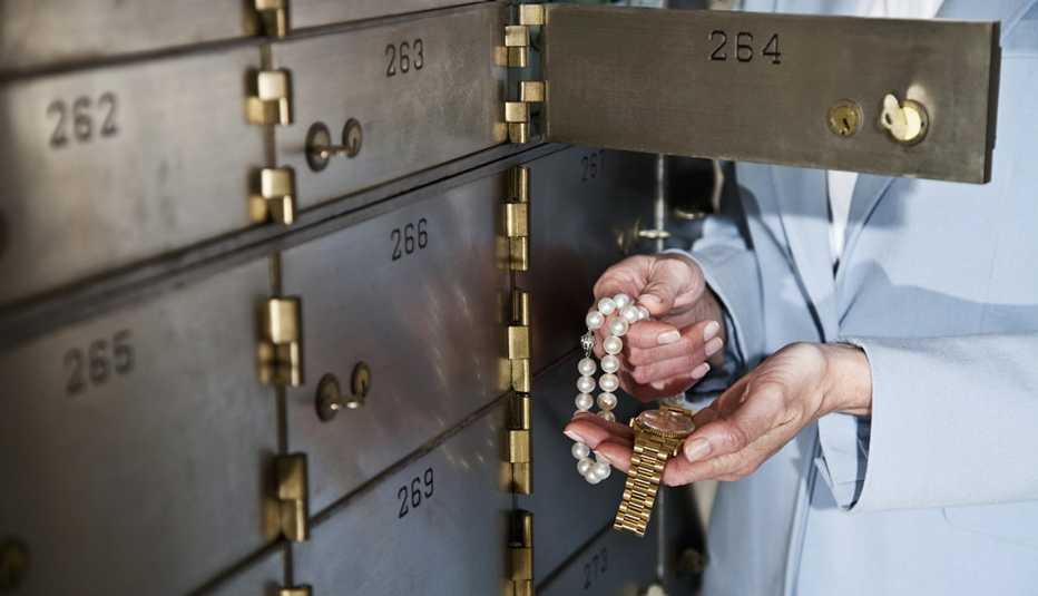 Woman holding necklace and gold watch, standing next to open safety deposit box
