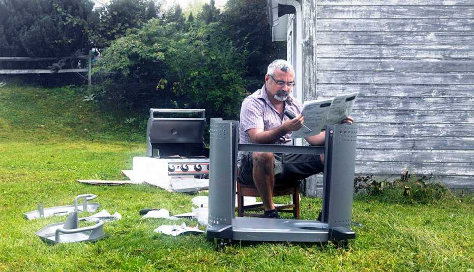 seated man in his backyard is looking at assembly instructions for a new barbeque grill 