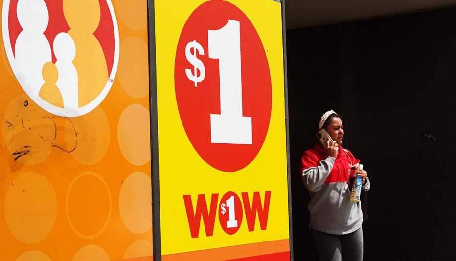 A customer exiting a dollar store that has a yellow and red one dollar "wow" poster in the window.