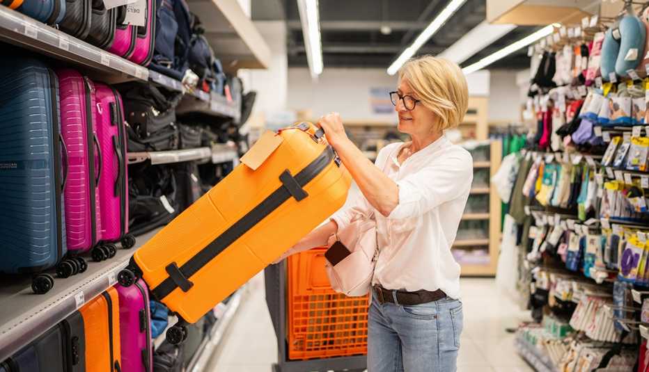 A woman selects a bright orange suitcase from the luggage aisle of a store.