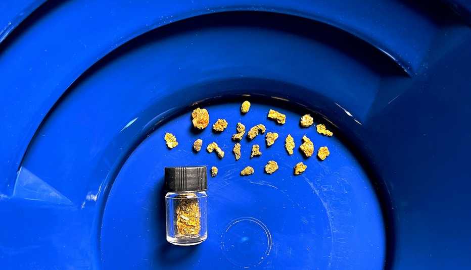 plastic pan used for panning for gold containing some gold flakes and a small nugget in a jar