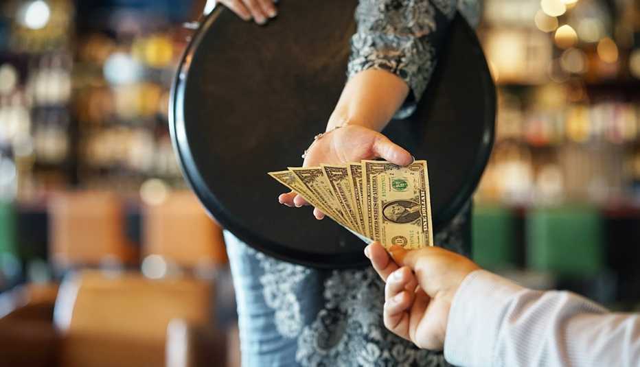 Closeup as a customer hands over five dollar bills to a server carrying a tray.