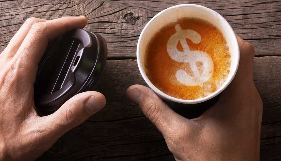 High angle close up of hands holding a mug of coffee with foam in the form of a dollar sign.