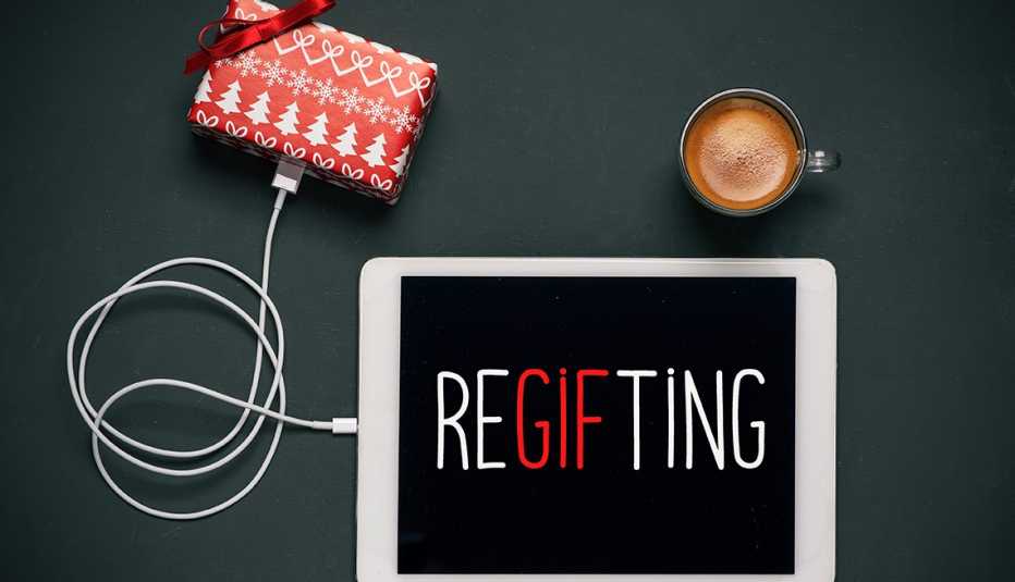 high-angle view of a tablet with the word regifting in its screen, connected to a gift by a cable, and a cup of coffee, placed on a dark gray table