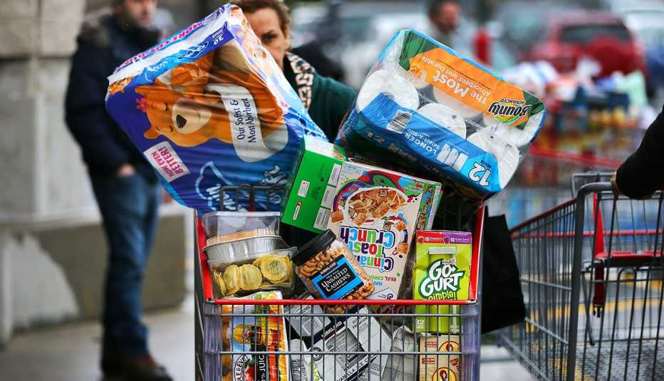A shopper is pushing a big cart of food and household staples including toilet paper, bottled water, diapers and canned goods outside a Costco warehouse.