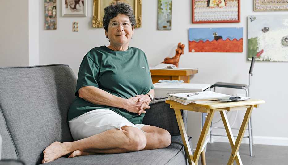 celia nathan sits on the couch in her home in maryland with lots of art on the wall