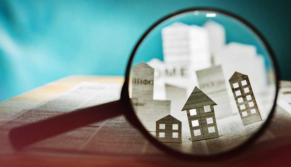 Magnifying glass examining paper cutouts of houses and news related to real estate and home buying and selling.