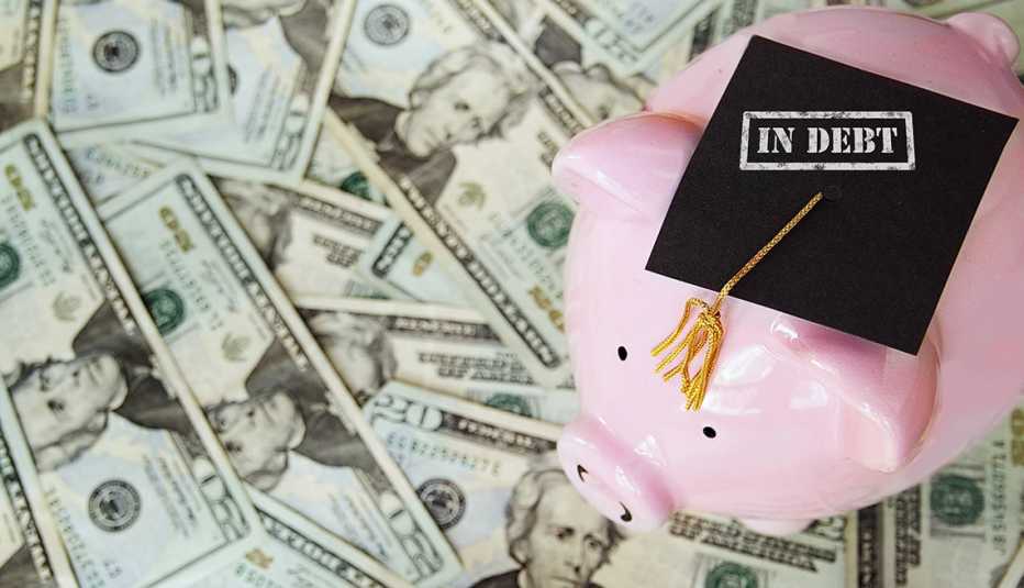 a   piggy bank wearing a graduation cap marked "debt" sits on a field of money