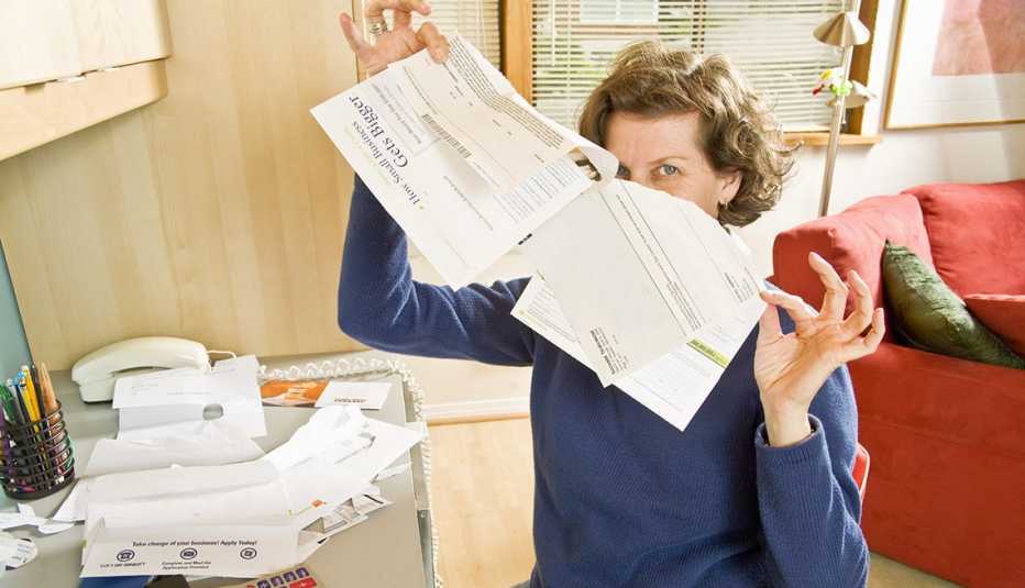woman seated in home office looks relieved as she rips up a bill from a big stack on her desk