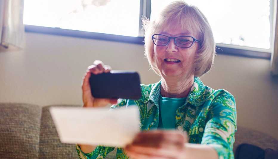 A smiling senior woman in her living room takes a picture with her smartphone of a check for digital electronic depositing