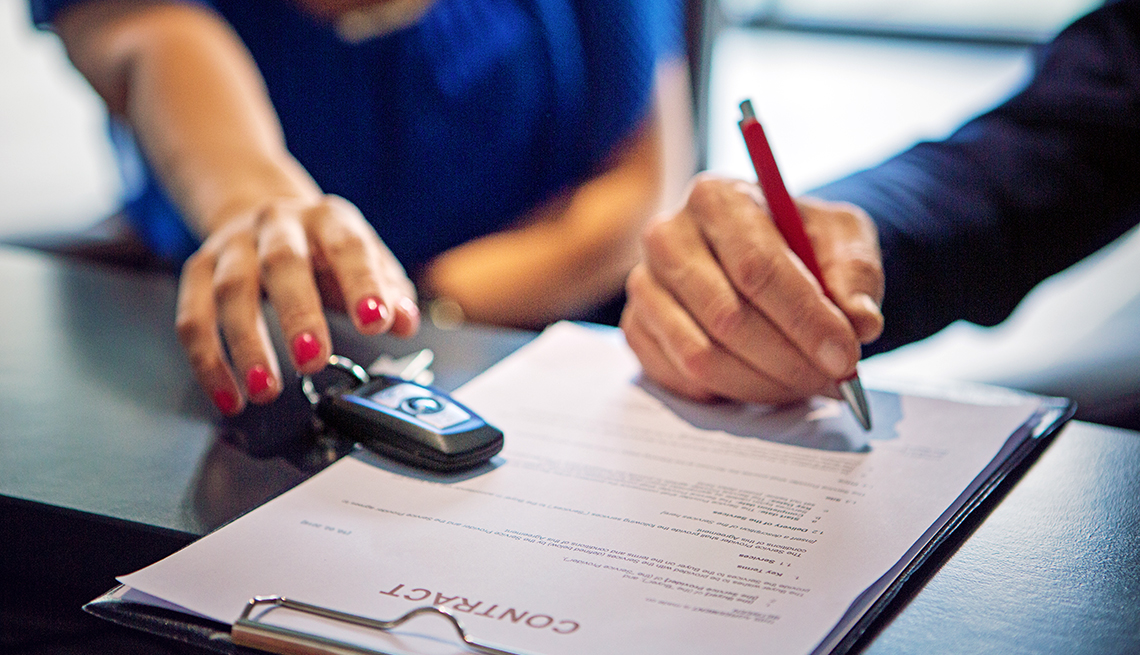 closeup of a woman's hand reaching over car keys as man's hand is signing a contract 