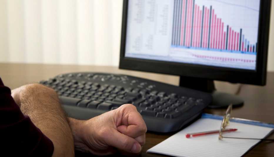 a man clenches his hands in stress while looking at falling stocks on a computer monitor