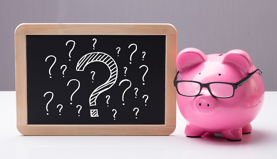 a pink piggy bank with black glasses next to a chalkboard with question marks on it
