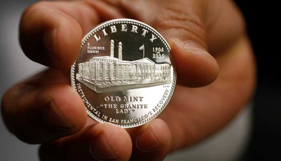 A hand is holding up to the camera, a silver commerorative coin, showing the Old Mint in San Francisco.