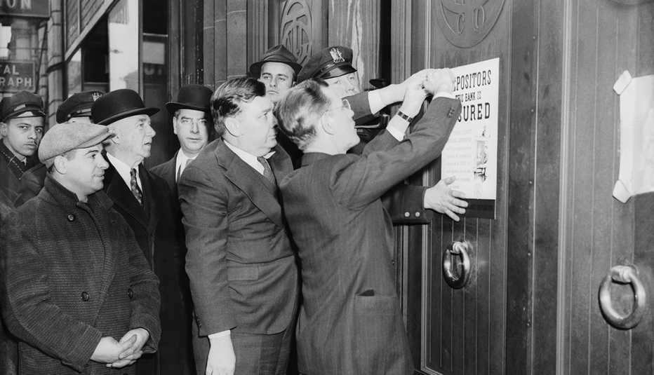 A historic photo shows people watching as a notice from the Federal Deposit Insurance Corporation is tacked on the door of a failed New Jersey bank in 1939, assuring investors that most deposits are protected.