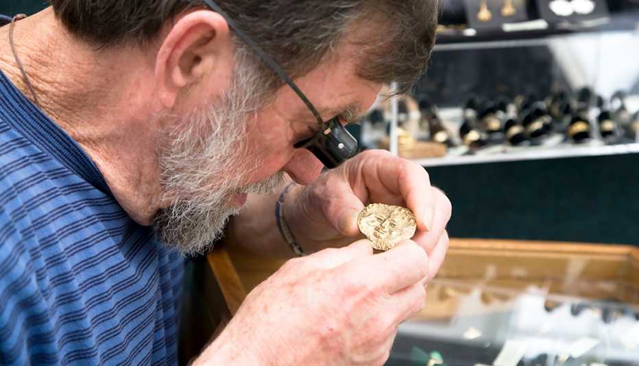 A man is using a jewelers' magnifying loupe to closely examine a piece of gold jewelry