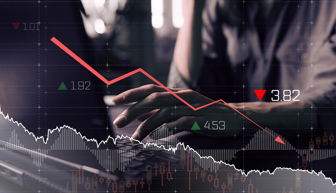 a double exposed image shows a downtrend financial chart superimposed over a black and white photo background of an investor's hands on a computer keyboard