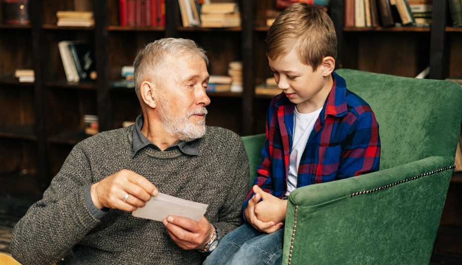 Grandfather talking with grandson at home in a room with background of bookshelves.