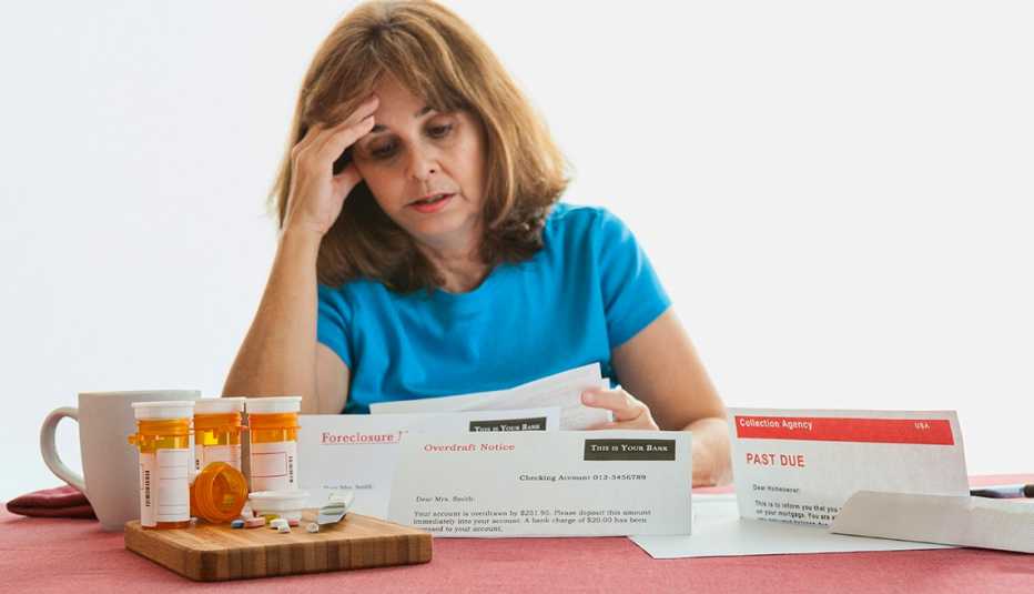 A senior woman looks at past due bills spreas across a table along with prescription medicine containers. 