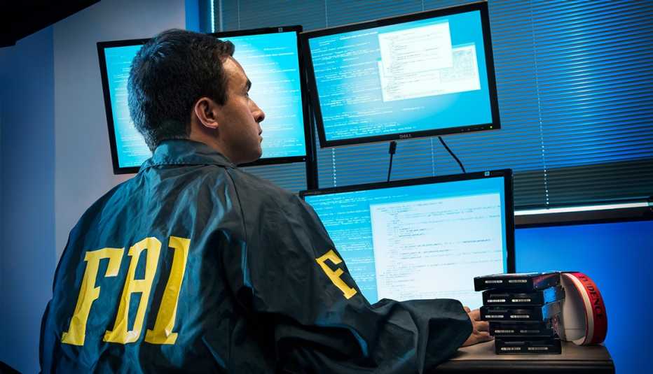 A man with a FBI logo jacket sits in front of computer screens
