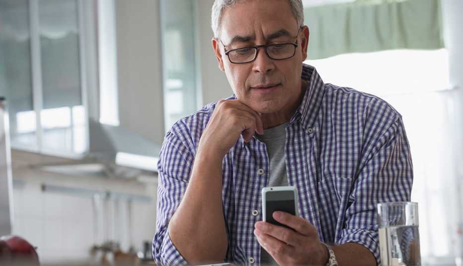 Hispanic man using cell phone in kitchen to read text message