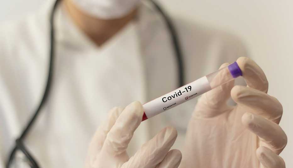 masked and gloved health care worker handing a vial labeled covid 19