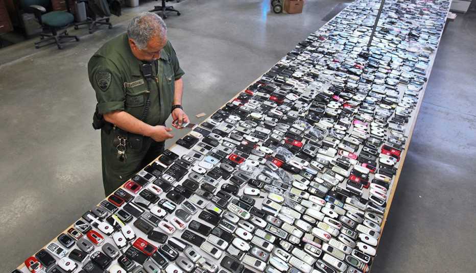 a prison guard inspects a long table entirely covered with contraband cellphones confiscated  from inmates