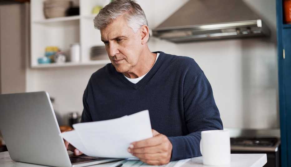 Man reviewing paperwork in kitchen on his laptop