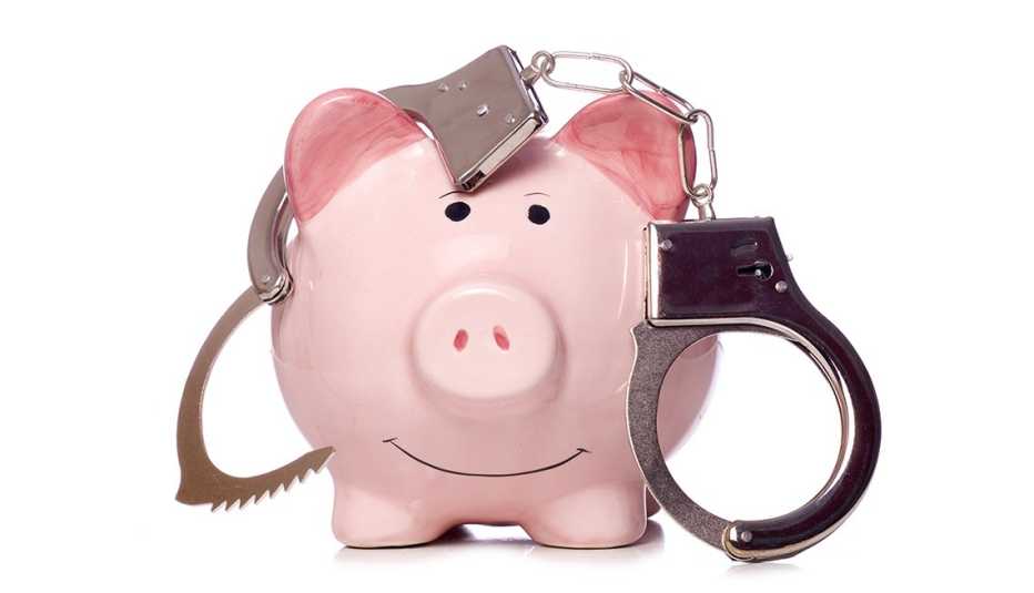smiling piggy bank draped in a pair of handcuffs against white background