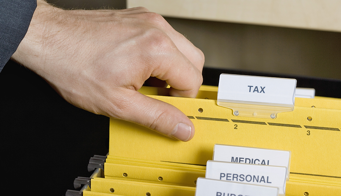 man pulling a folder labeled taxes out of a file drawer