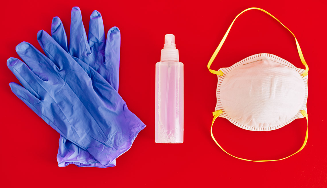 Protective mask, medical gloves and hand sanitizer displayed on red background