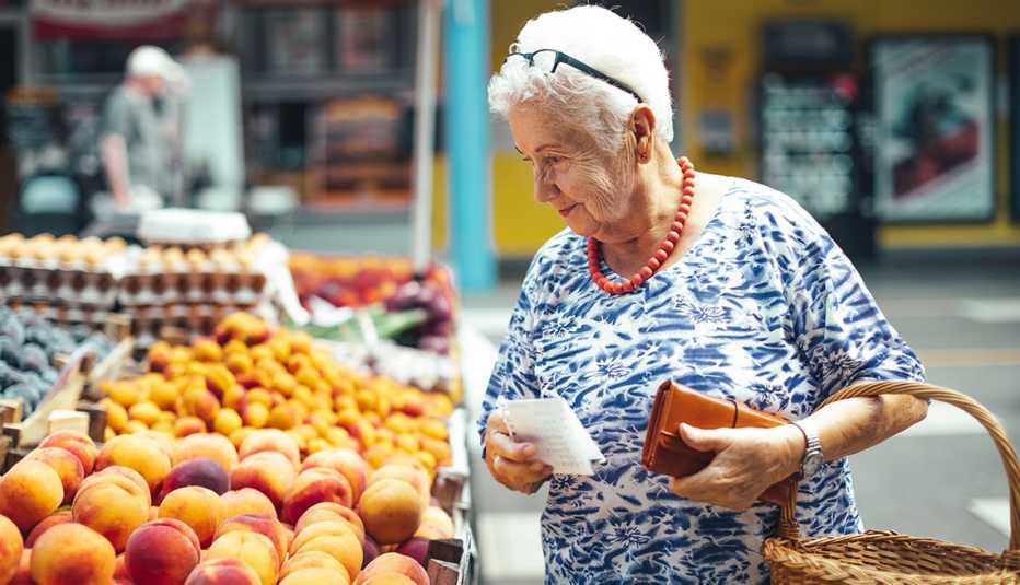 woman with shopping list and wallet examines fruit  for sale at outdoor produce market