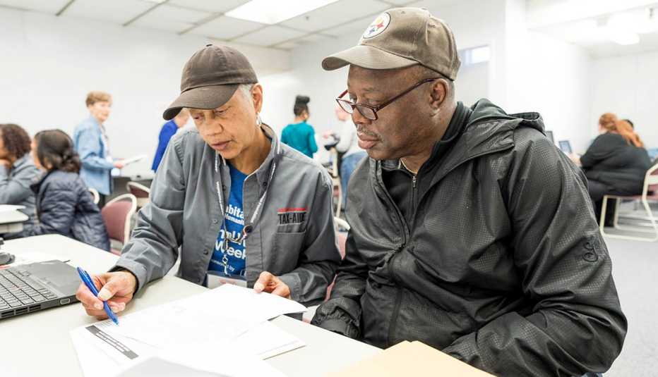 An A A R P tax aide volunteer helps a man look through his tax filing paperwork 