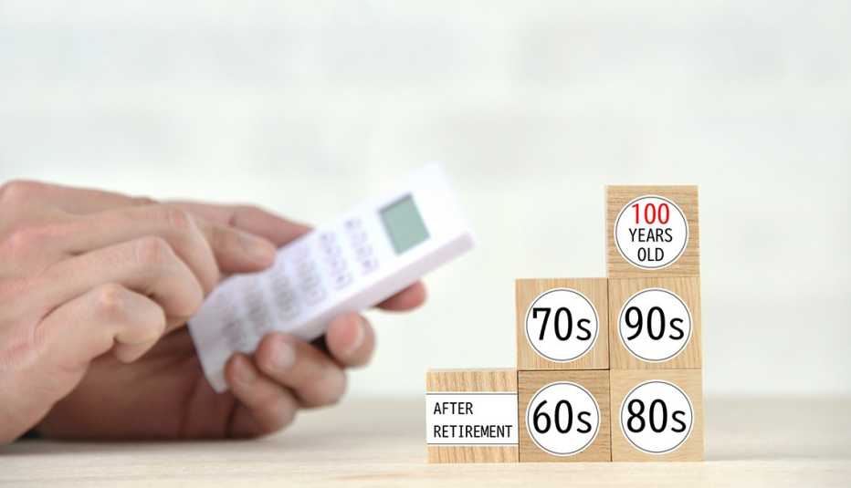 Close up of hands using a calculator next to a stack of wooden blocks marked with decades of age from "after retirement" to "100 years old".