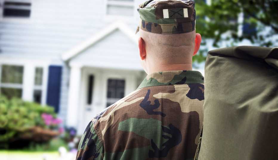 the back of a service member carrying duffel as he returns home and walks to front door 