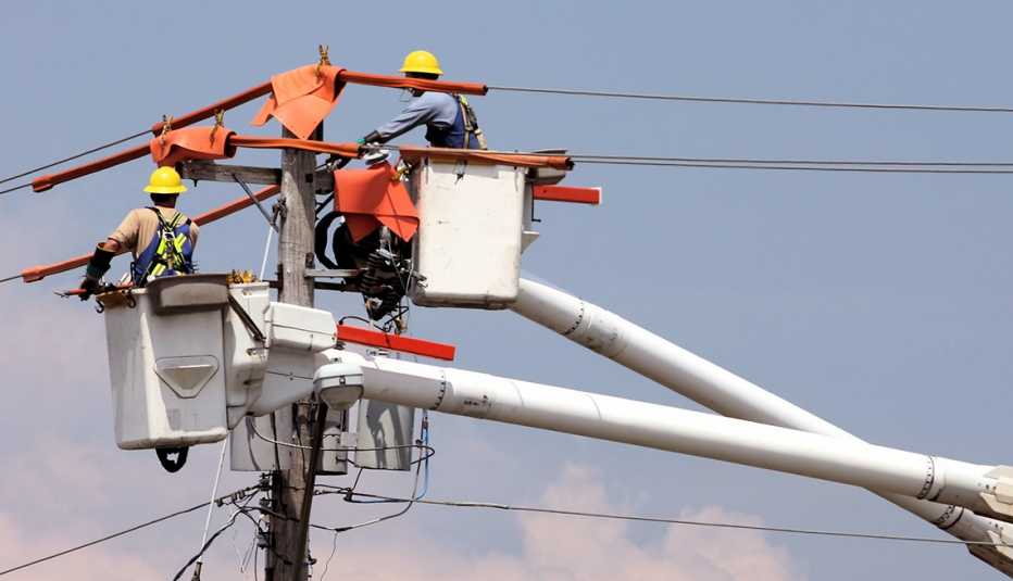 Two utility workers in a crane repairing a power pole
