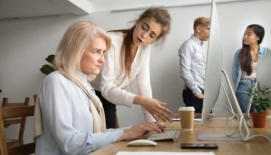 A woman working at a computer being scolded by a younger worker.