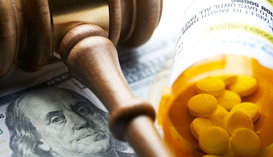A gavel on money next to a prescription bottle with pills
